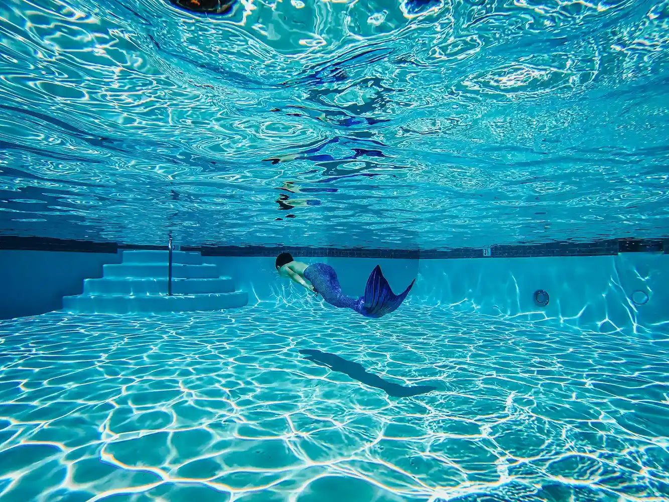 Mermaid Boy swimming underwater in a pool with clear blue water.