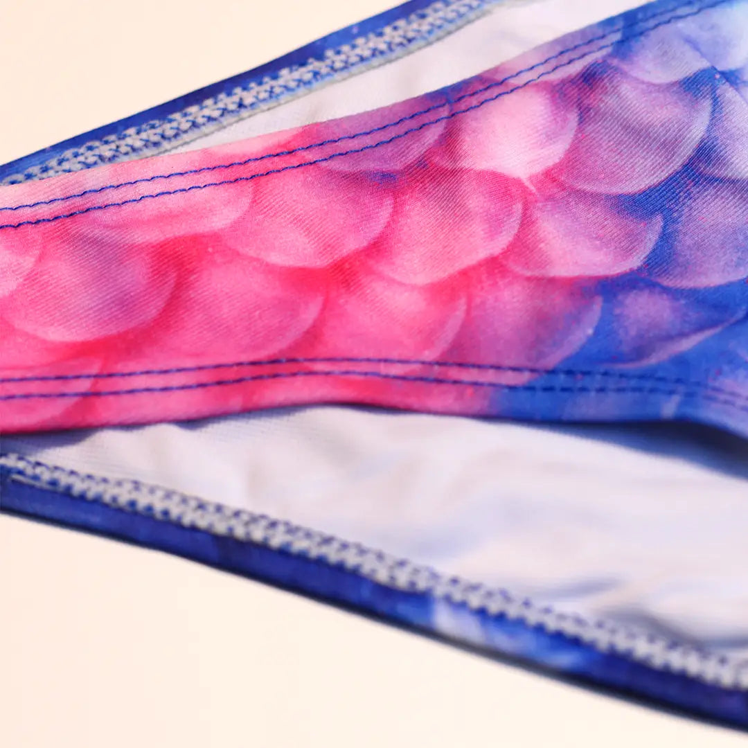 Detail front Studio product photography of Bikini bottom featuring a blue and pink galaxy fish scales print, part of the Ocean Queens Lunar Swim Brief collection