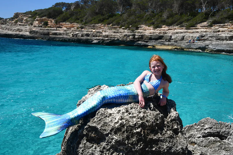 Girl on holiday with Ocean Queens mermaid tail on a rock at the sea. Real life photography of happy customer